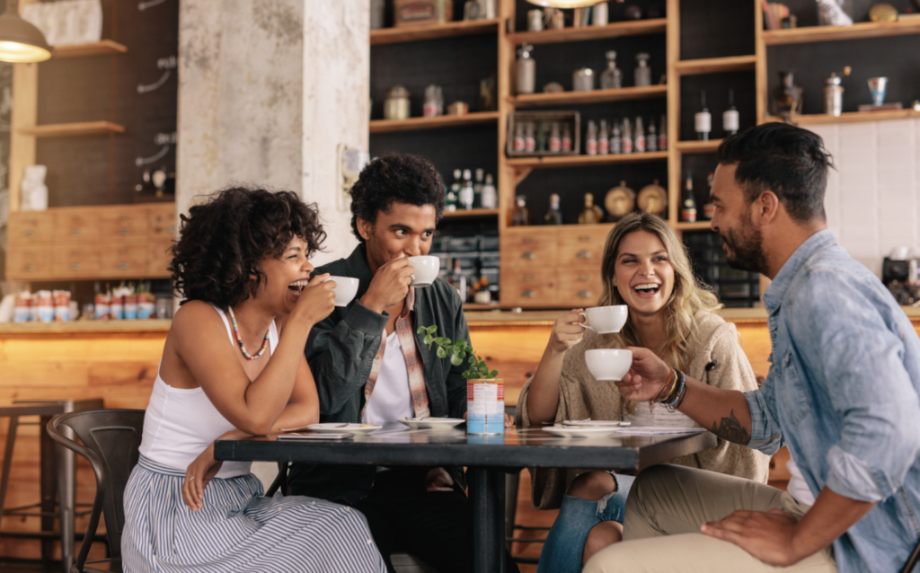 Friends laughing and drinking coffee together at a cozy café table.